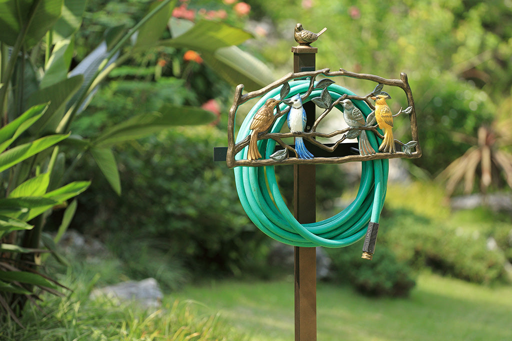 Garden hose holder with decorative birds in a garden setting