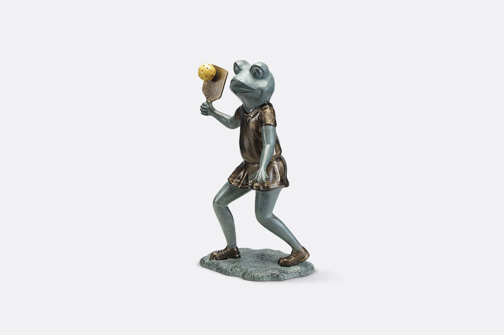 Sculpture of a frog holding a paddle playing pickleball.