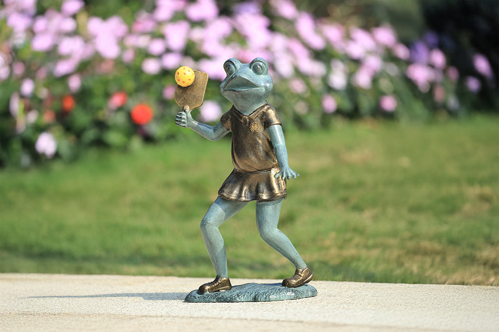Sculpture of a frog holding a paddle playing pickleball.