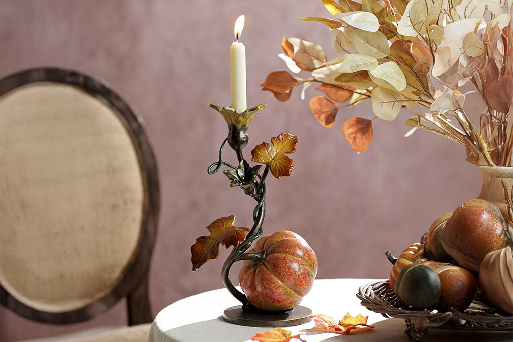 A candleholder statue of a blooming vine with a single pumpkin placed on a festive table.