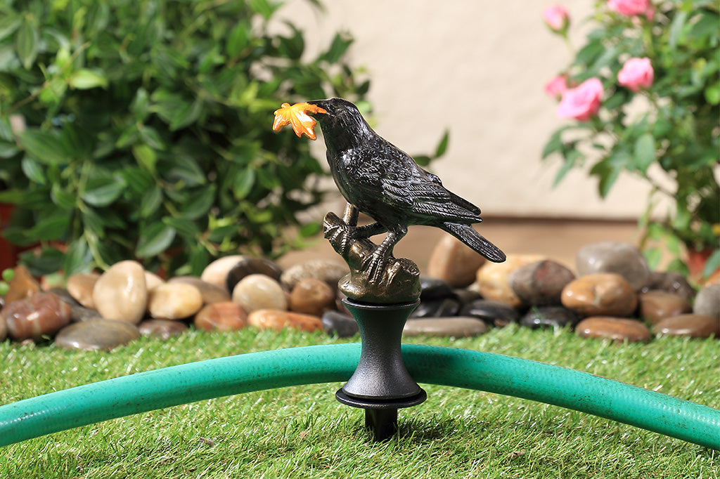 Decorative hose guard with a bird holding a leaf placed in a garden.