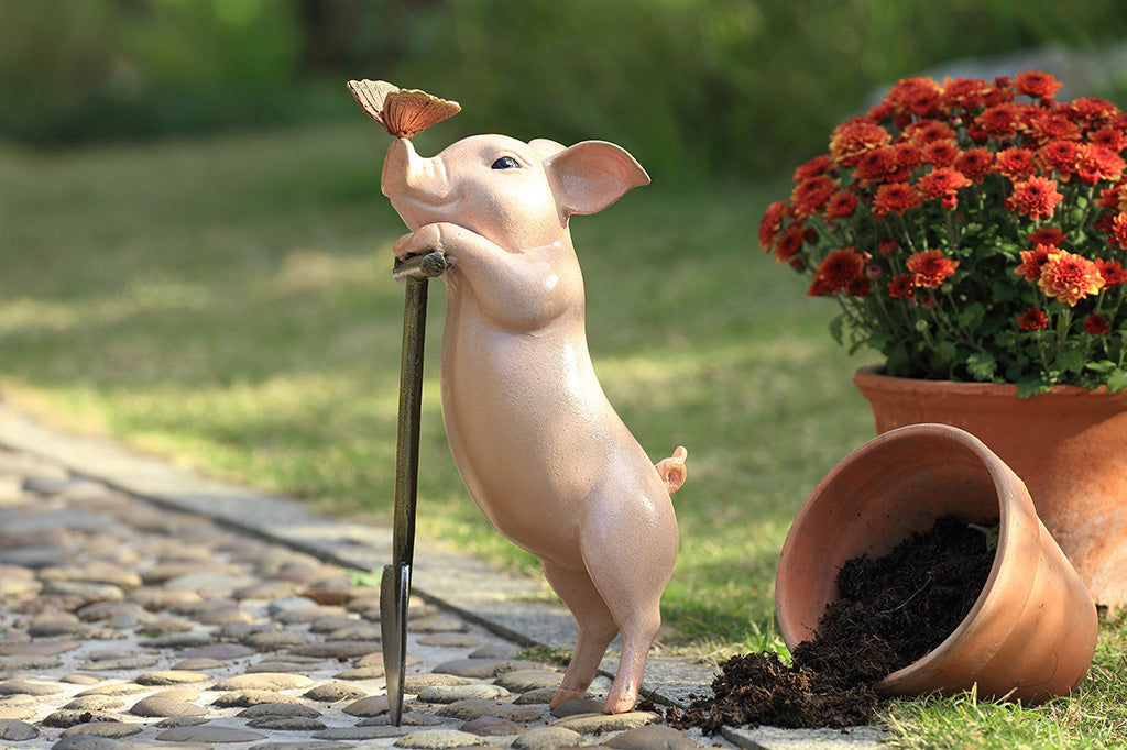 A sculpture of a pig holding a shovel with a butterfly landing on it's nose.