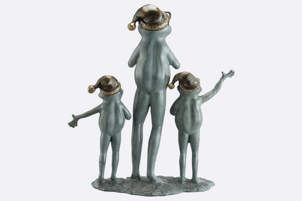 The back of a sculpture of a frog family with santa hats singing carols on a white background