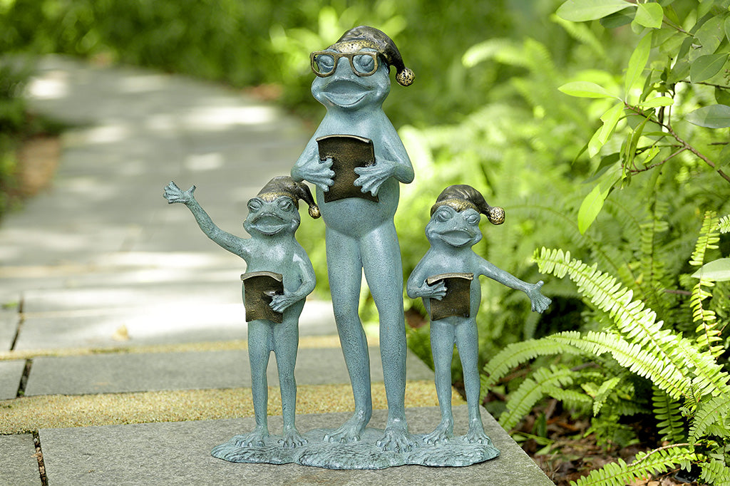 A sculpture of a frog family with santa hats singing carols placed in a garden path.
