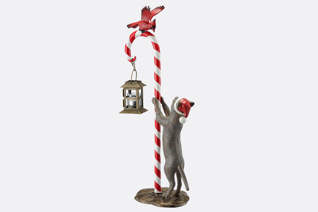 Decorative sculpture of a cat climbing a candy cane with a bird on top, on a white background.