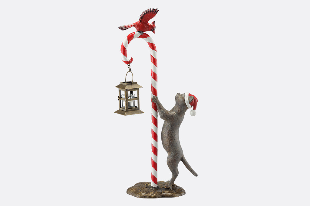 Decorative sculpture of a cat climbing a candy cane with a bird on top, on a white background.
