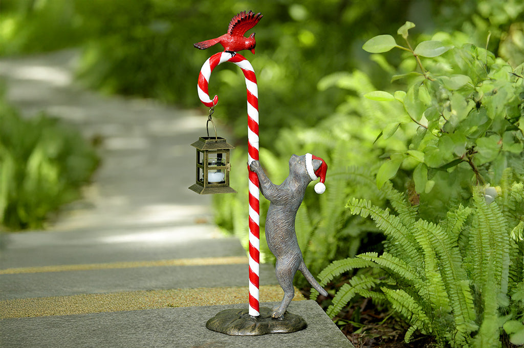 Decorative garden sculpture of a cat with a candy cane and lantern, set against a natural background.