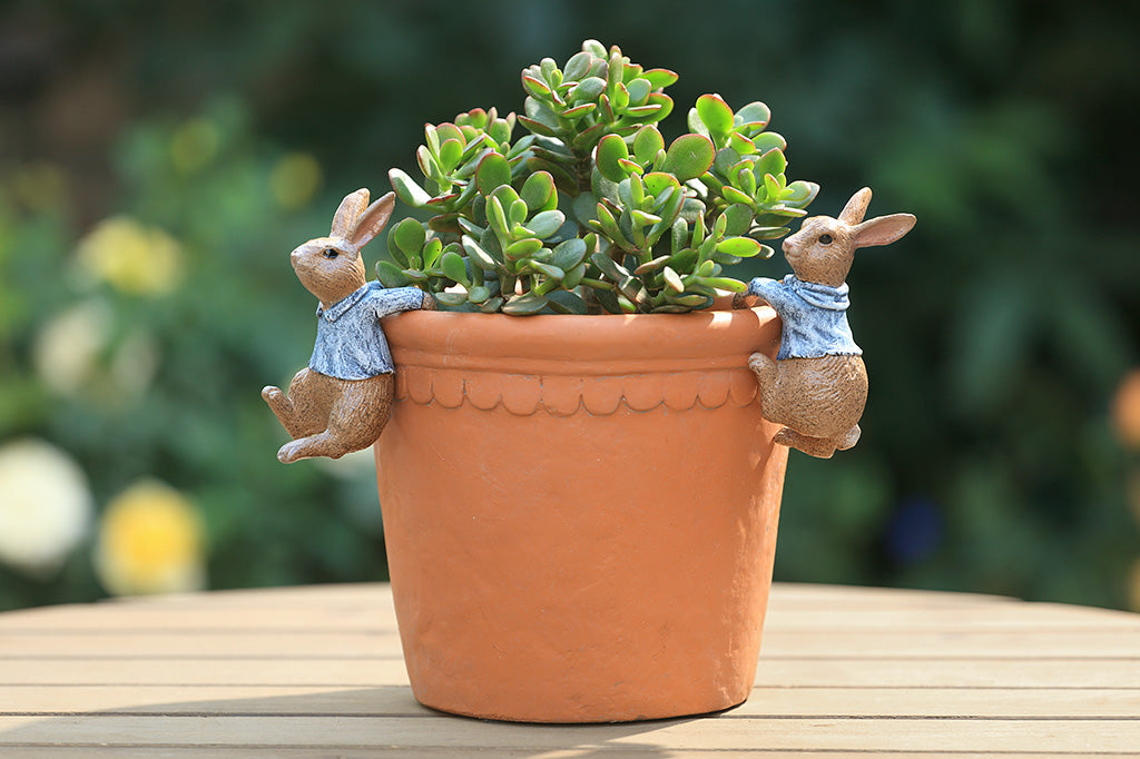 A hanging sculpture of two bunnies wearing blue shirts that dangle off of plant pots.