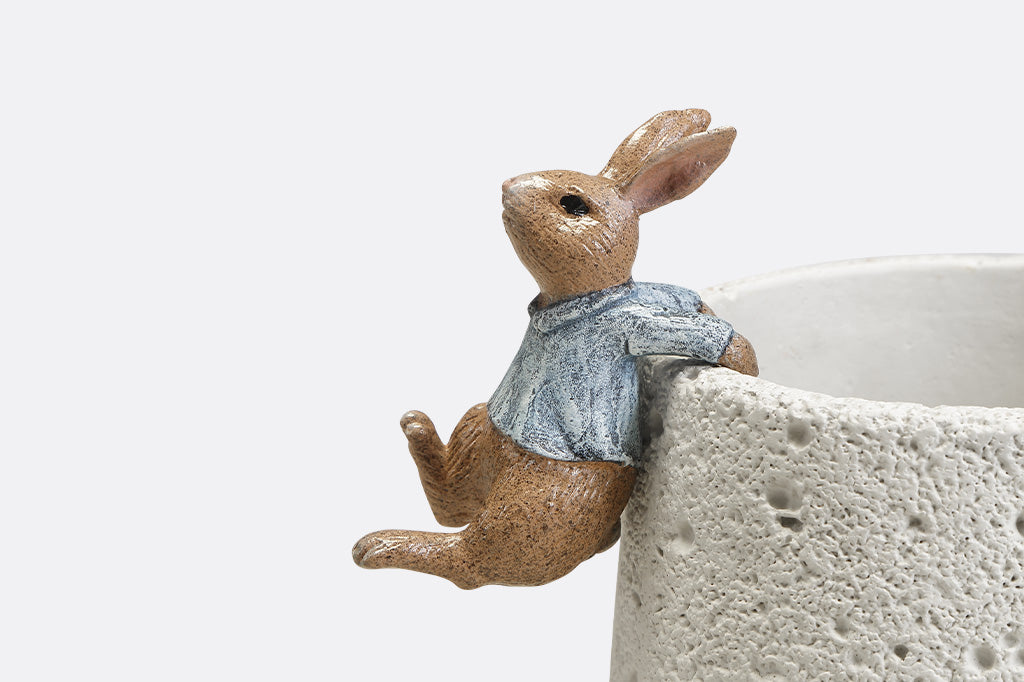 A hanging sculpture of two bunnies wearing blue shirts that dangle off of plant pots.