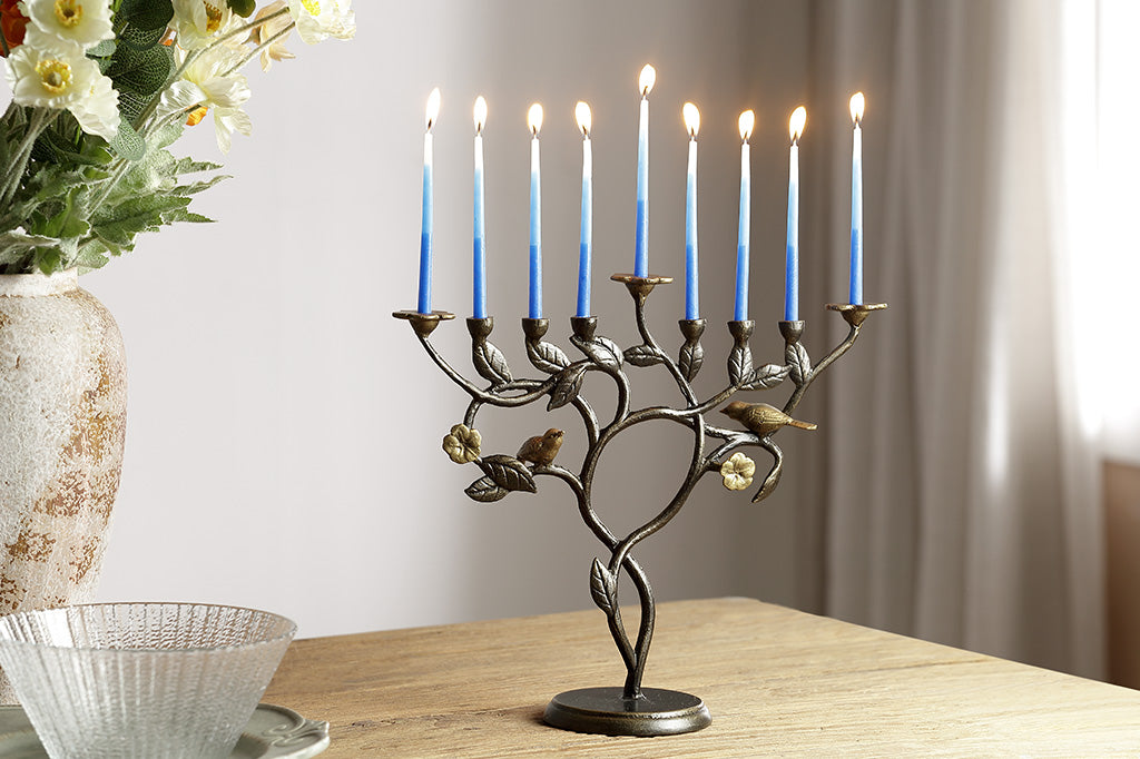 Menorah with lit candles on a table next to a vase of flowers.