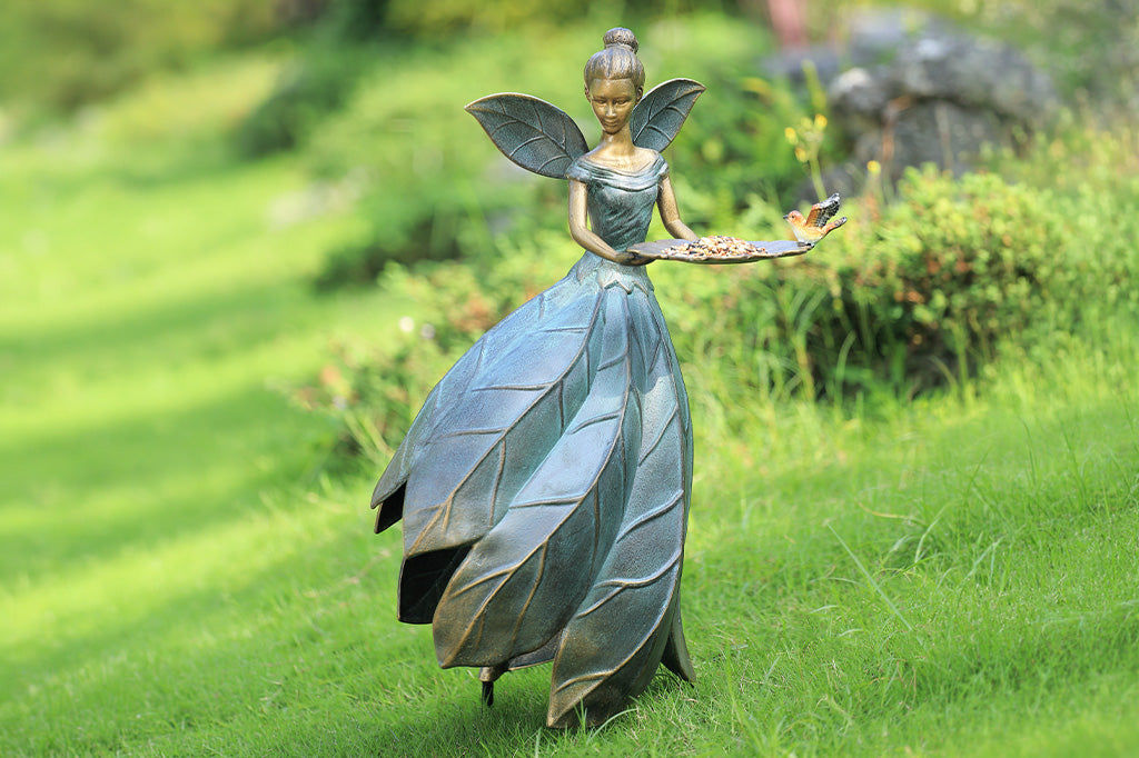 Statue of a fairy with leaf-like wings and dress on grass, held up by removable stakes