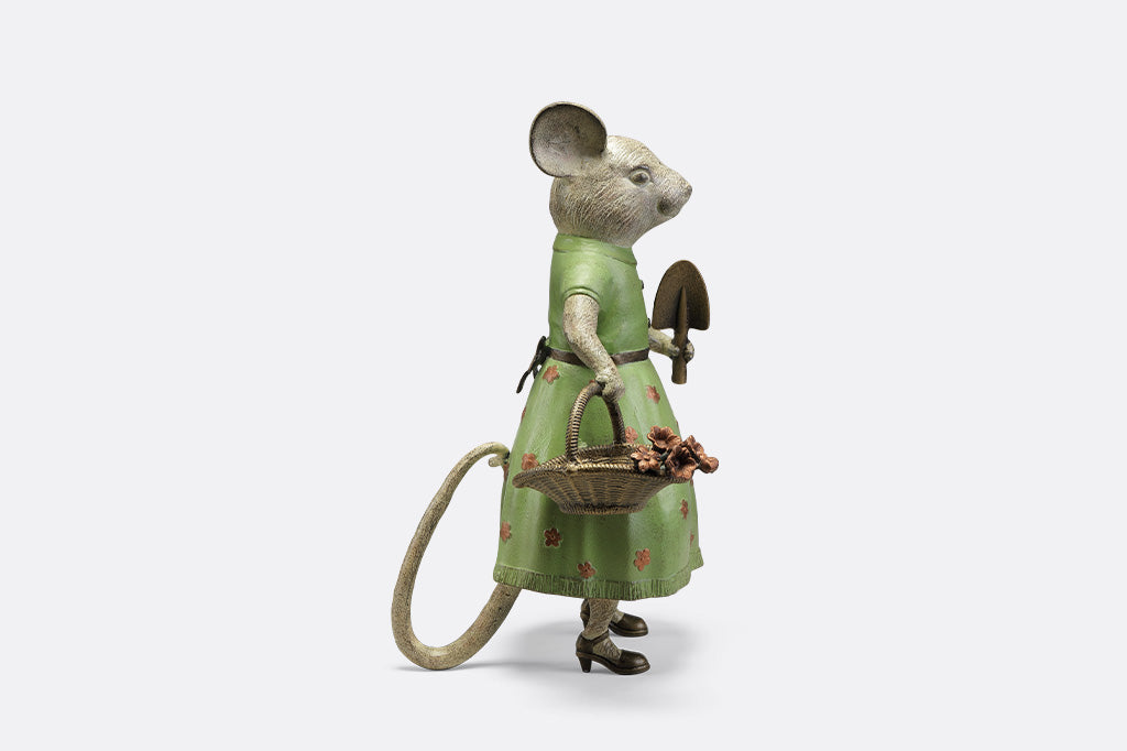 A mouse in a green dress holding a shovel and a basket of flowers.