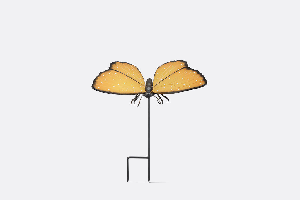 Butterfly-shaped garden stake with orange wings and black body on a white background