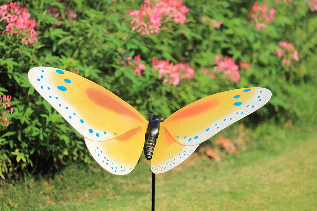Yellow and orange butterfly garden stake with blue dots in a garden