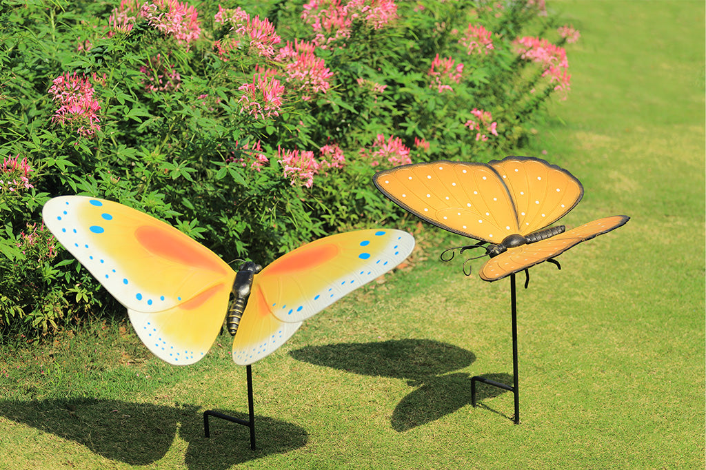 Two butterfly garden stakes in a garden, one with blue dots and the other with white dots and orange background