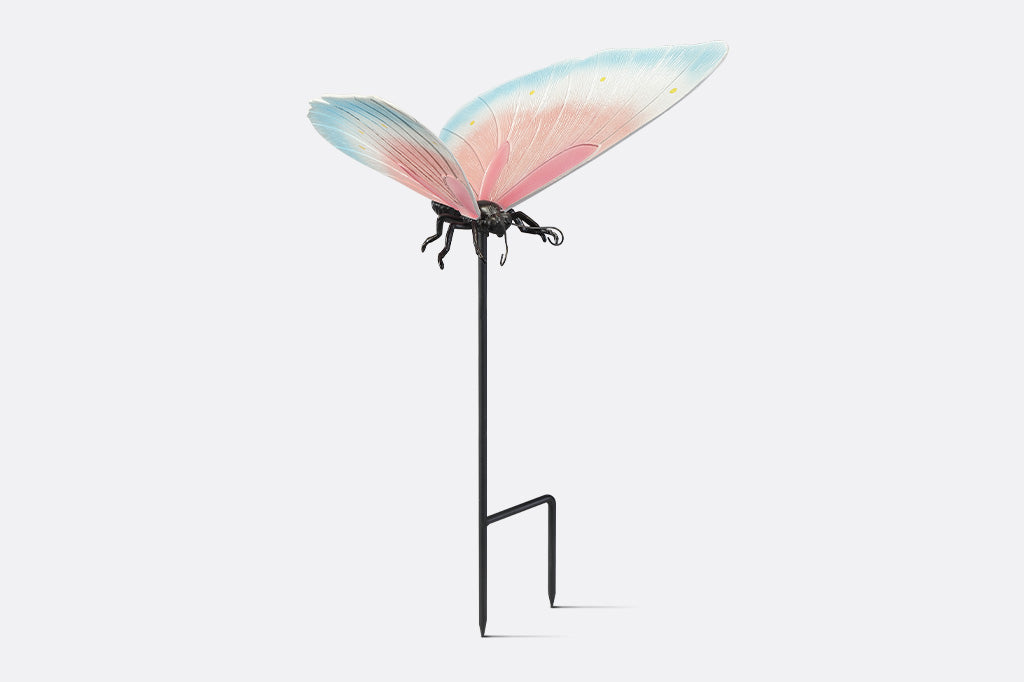 A garden stake sculpture of a butterfly with hues of light blue, white, and pink with yellow details.