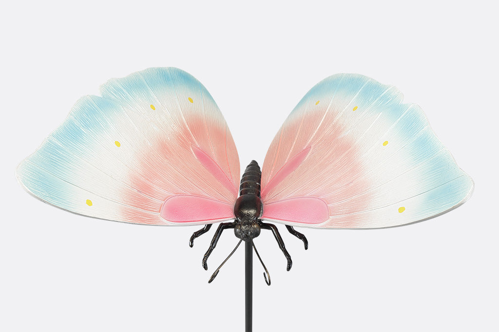 A garden stake sculpture of a butterfly with hues of light blue, white, and pink with yellow details.