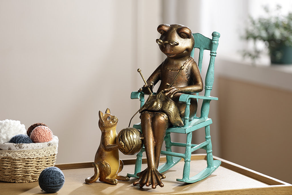 Sculpture of a frog knitting on a chair with a Cat and yarn ball