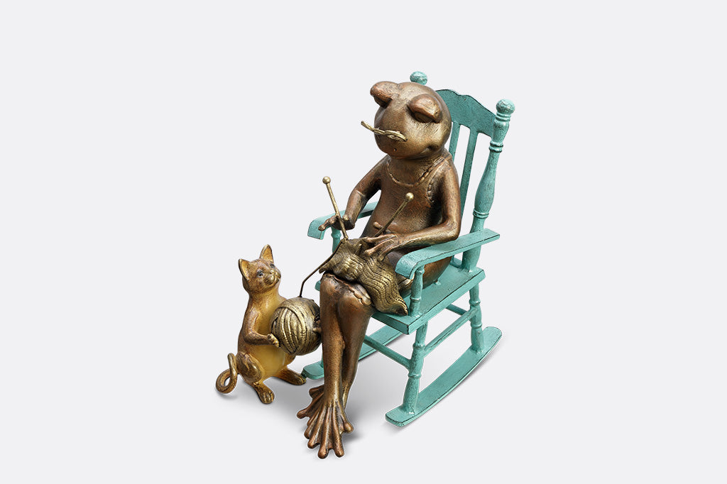 Sculpture of a frog knitting on a chair with a Cat and yarn ball on a white background