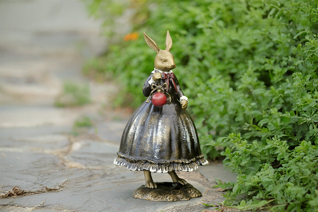 Sculpture of a bunny dressed in Victorian Era attire holding a red Chirstmas ornament. 