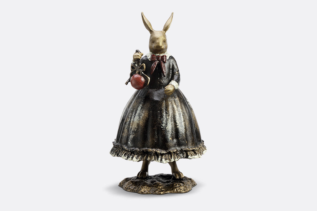 Sculpture of a bunny dressed in Victorian Era attire holding a red Chirstmas ornament. 