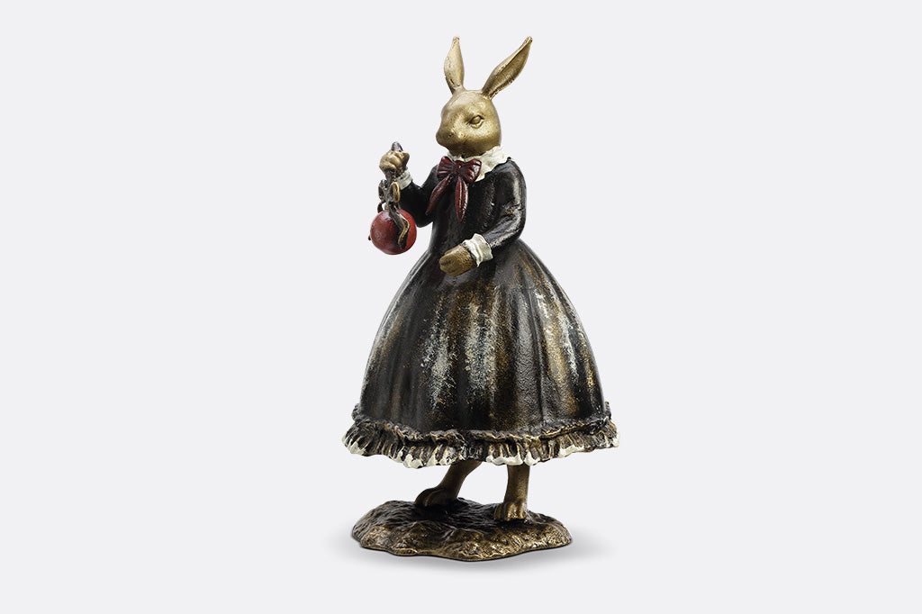 Sculpture of a bunny dressed in Victorian Era attire holding a red Chirstmas ornament. 