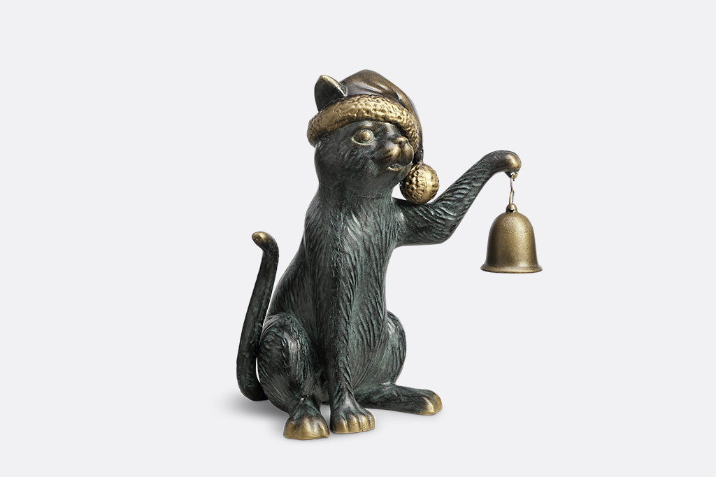 Cat figurine wearing a hat and holding a bell on a white background