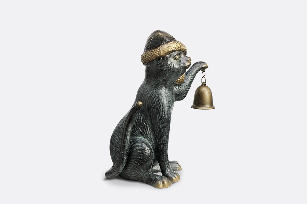 Cat figurine wearing a hat and holding a bell on a white background