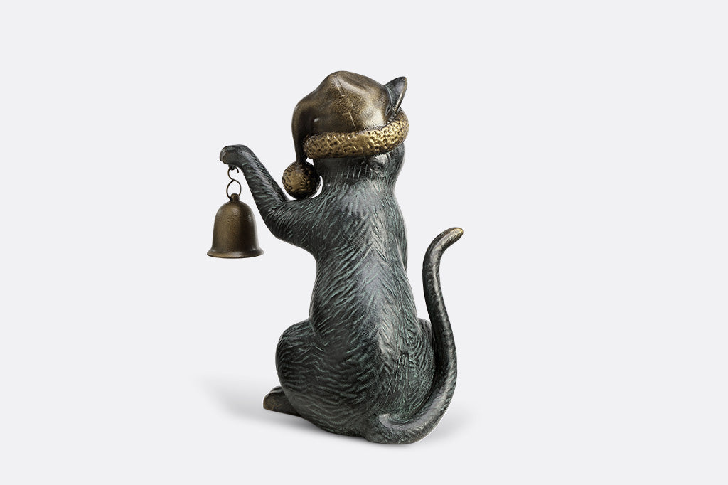 Cat figurine wearing a hat and holding a bell on a white background