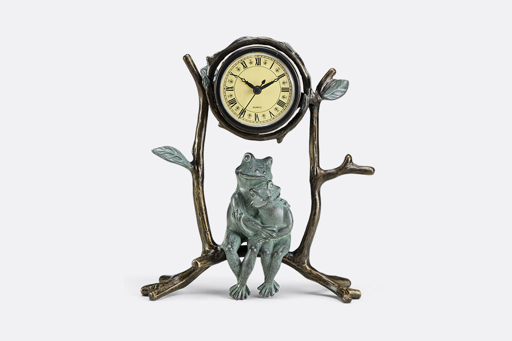 A clock with a sculpture of two frogs hugging while sitting on branches.