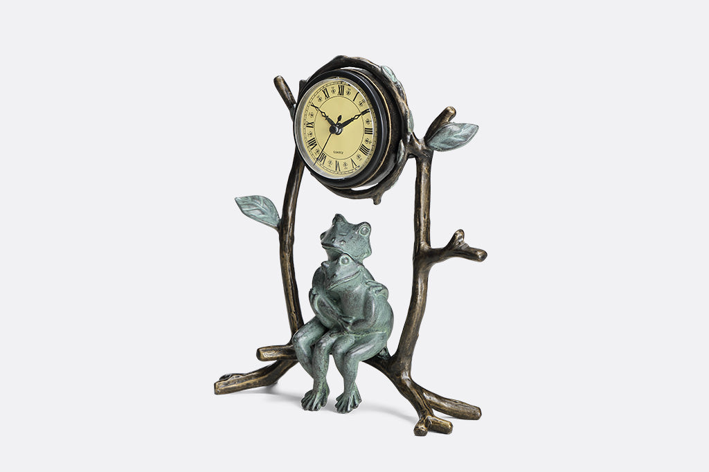 A clock with a sculpture of two frogs hugging while sitting on branches.
