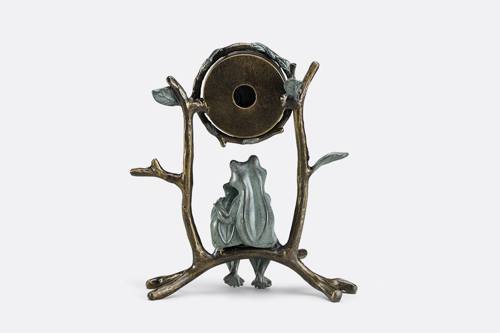A clock with a sculpture of two frogs hugging while sitting on branches.