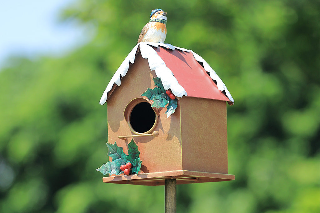 A holiday themed birdhouse with a bird wearing a knitted cap and scarf.