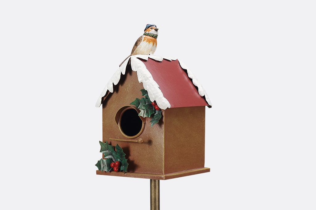 A holiday themed birdhouse with a bird wearing a knitted cap and scarf.