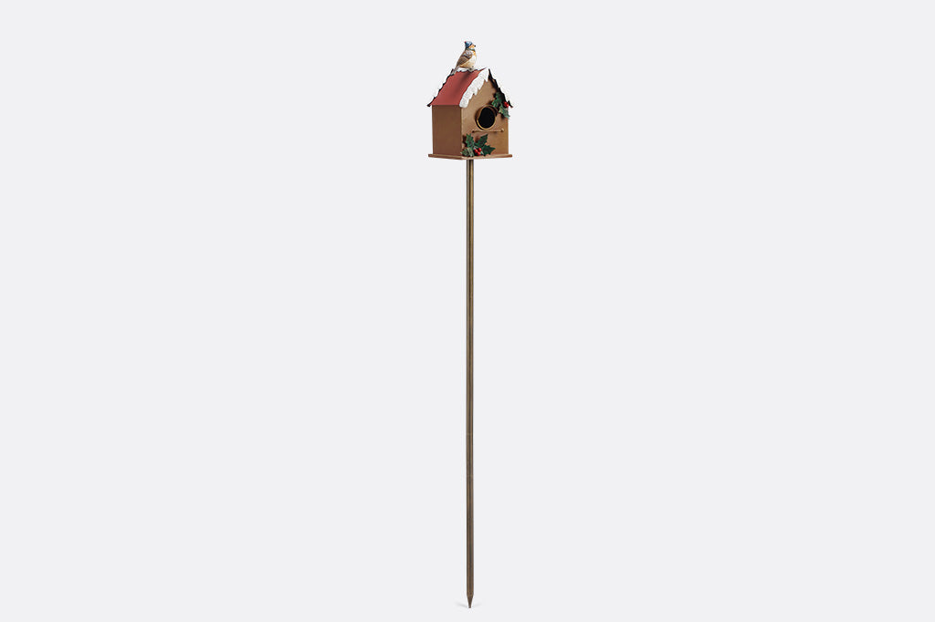 A holiday themed birdhouse with a bird wearing a knitted cap and scarf.