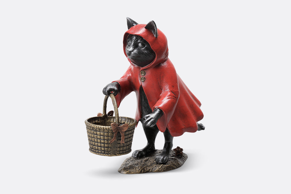Statue of a cat in a red hooded cloak holding a basket on a white background