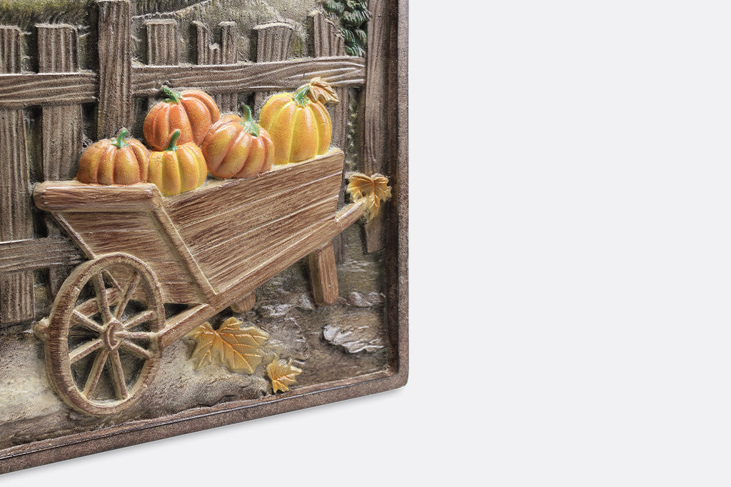 Decorative wall art with a wooden wheelbarrow and pumpkins against a rustic background.