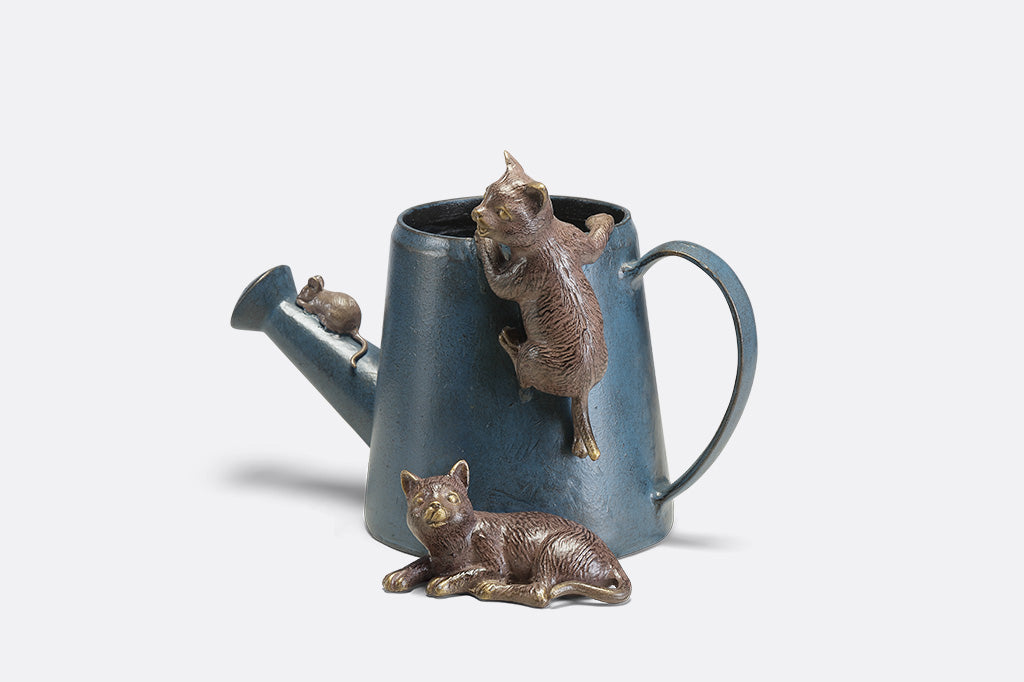 A decorative watering can planter with two cats climbing around to follow a mouse.