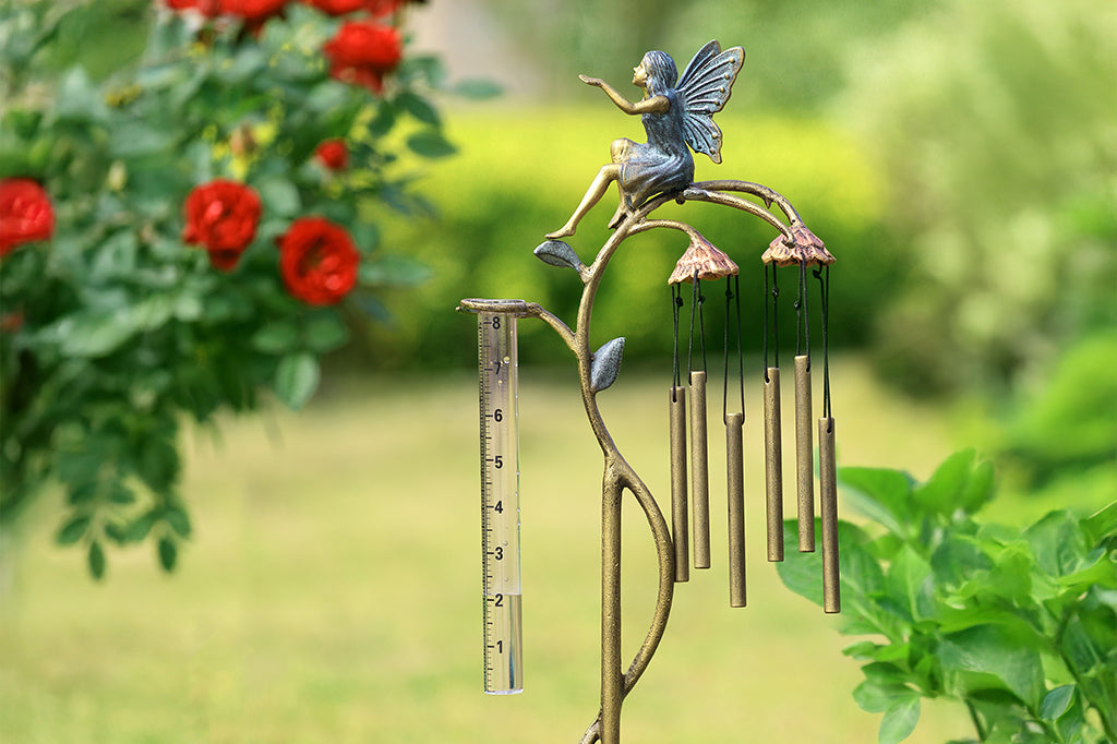 A staked raincatcher and windchime of a fairy sitting on flowers.