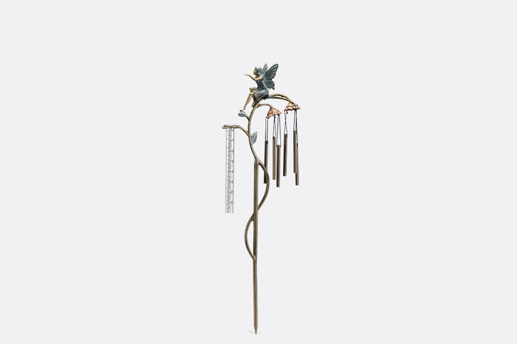 A staked raincatcher and windchime of a fairy sitting on flowers.