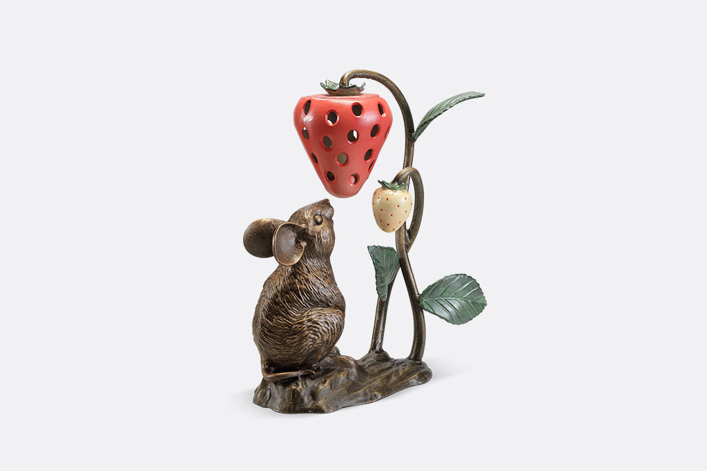 A sculpture of a mouse looking up at a strawberry shaped lantern.