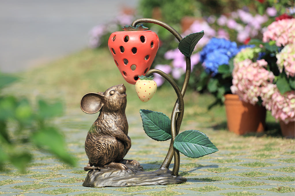 A sculpture of a mouse looking up at a strawberry shaped lantern.
