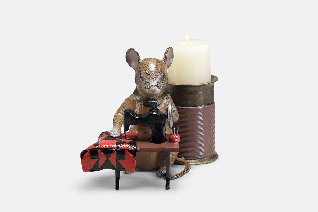 A candleholder of a mouse at a sewing machine stitching fabric.