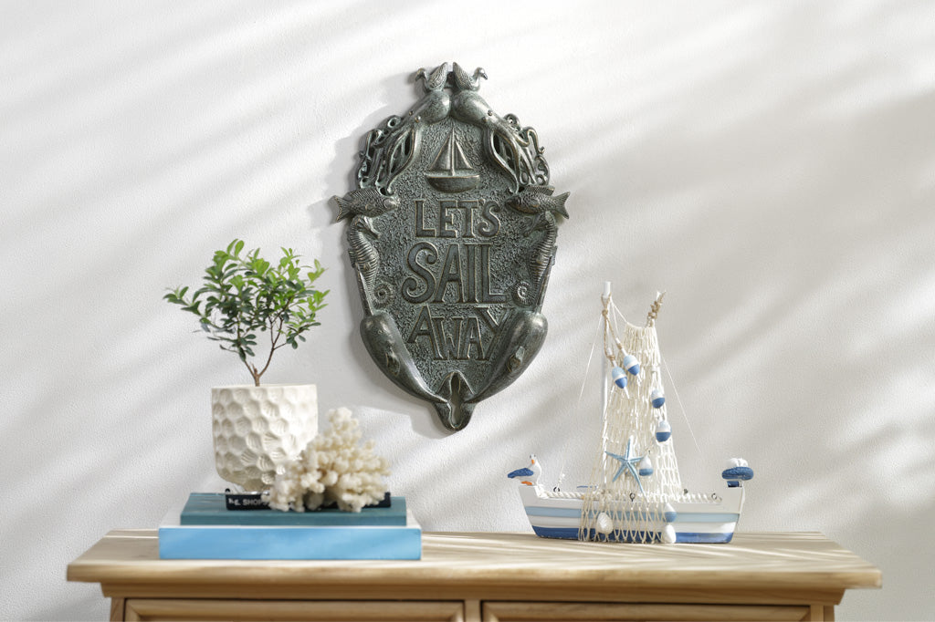 Decorative wall plaque with 'Let's Sail Away' text above a table with a model ship and plants.