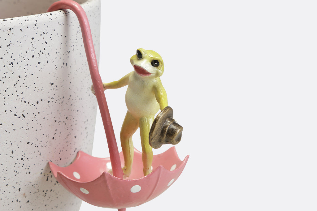 Pot hanging sculptures of dancing frogs inside of pink polka dot umbrellas.