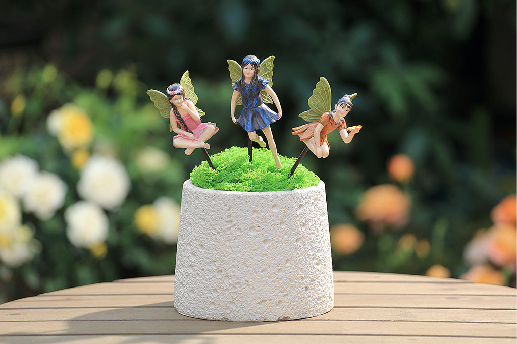 A trio of fairy sculpture plant pot stakes, one wearing pink, one wearing blue, and one wearing orange.