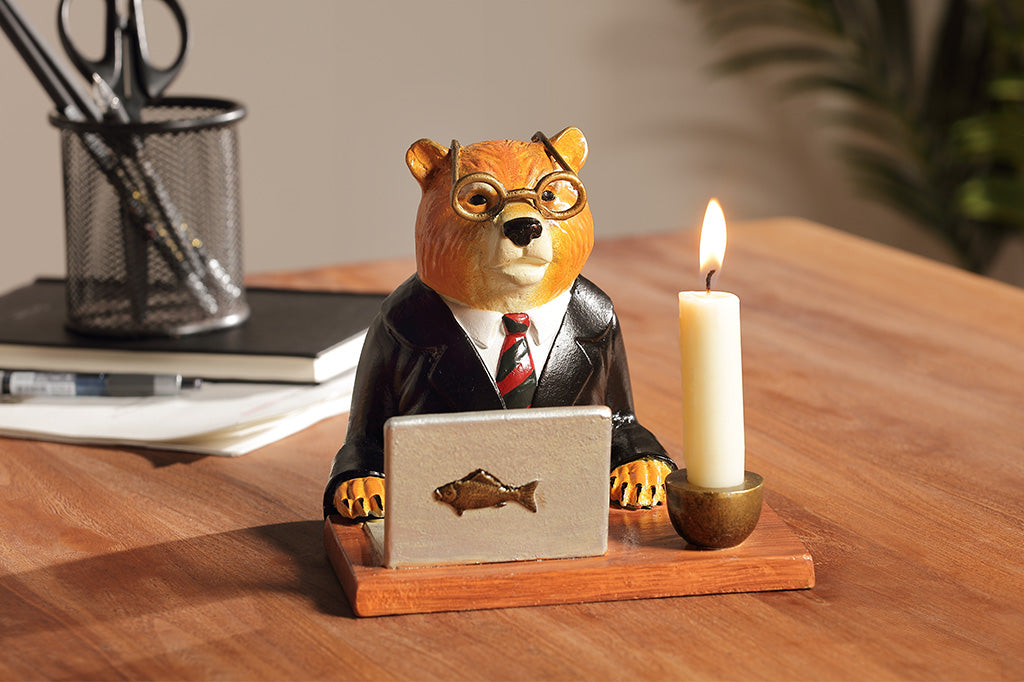 A sculpture of a bear wearing a suit on his Fishbook Pro laptop with a mug and candle.