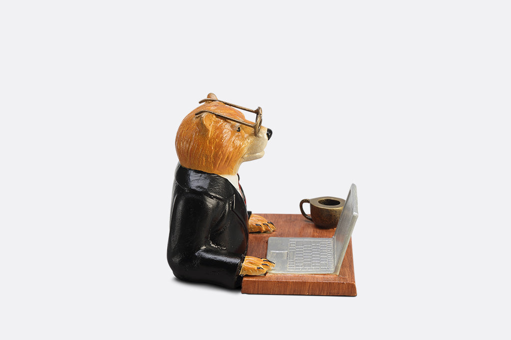 A sculpture of a bear wearing a suit on his Fishbook Pro laptop with a mug.