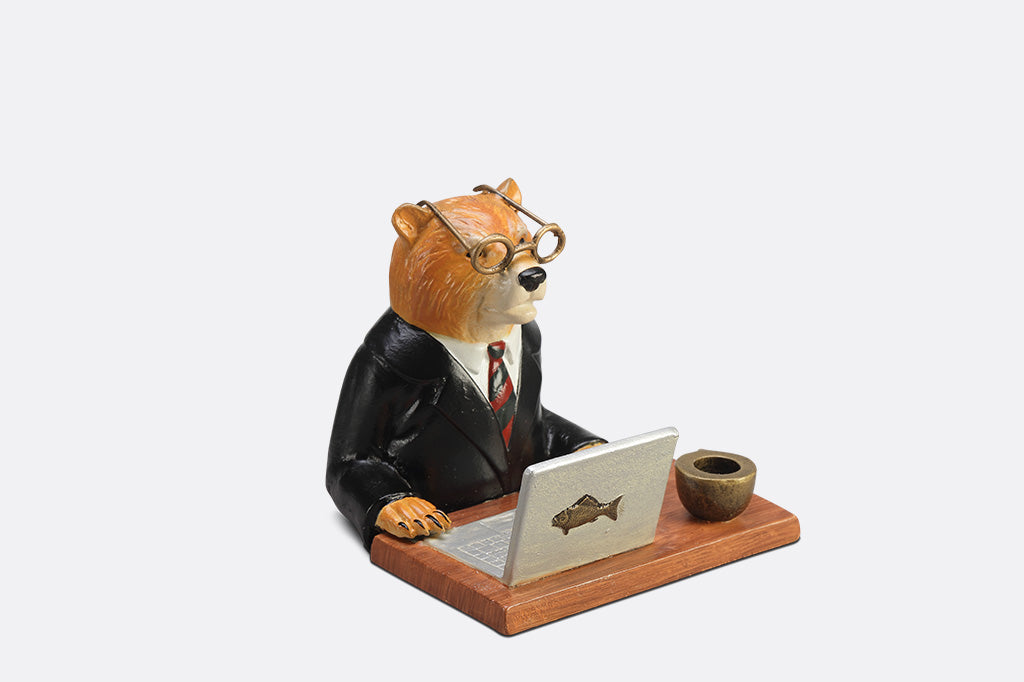 A sculpture of a bear wearing a suit on his Fishbook Pro laptop with a mug.