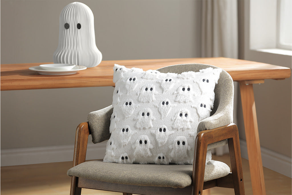 Decorative pillow with ghost pattern on a chair next to a table with a ghost-shaped object.